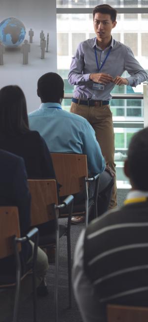 Young businessman speaking to business professionals sitting at seminar in office Young businessman speaking to business professionals sitting at seminar in office
